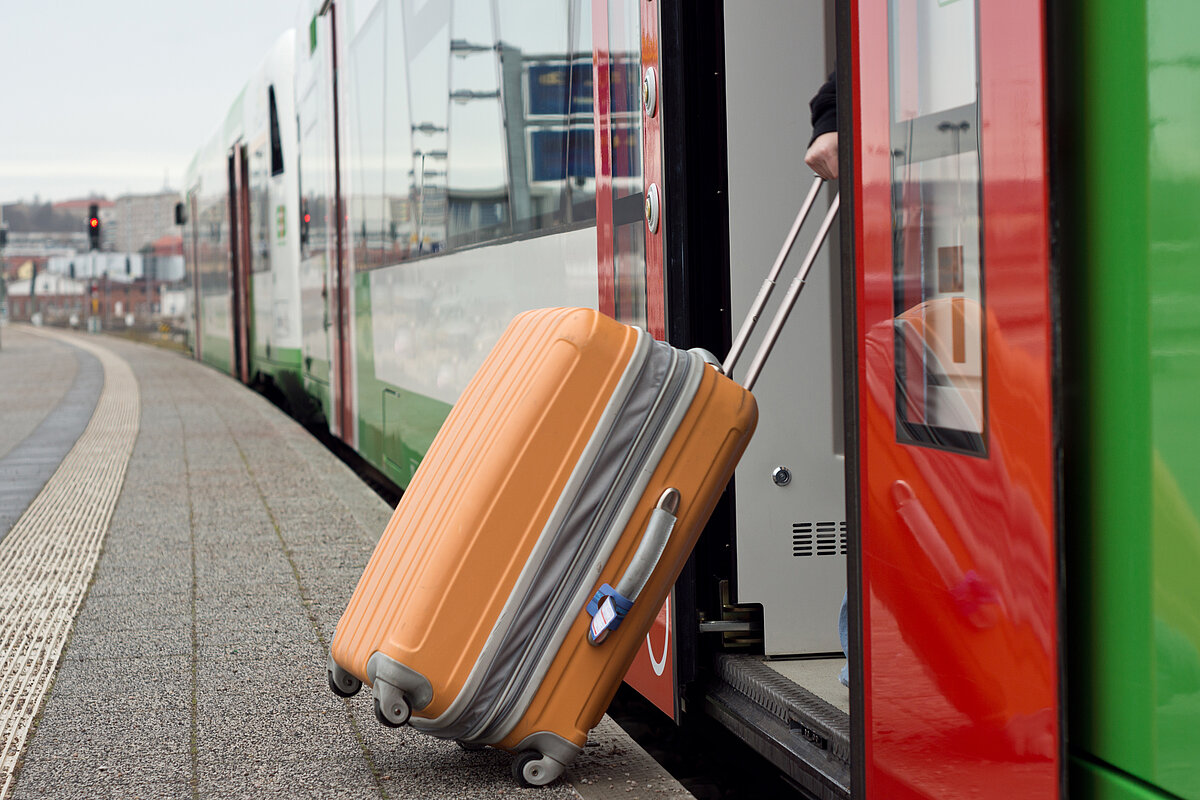 Eine Person steigt mit einem Rollkoffer in einen Zug ein