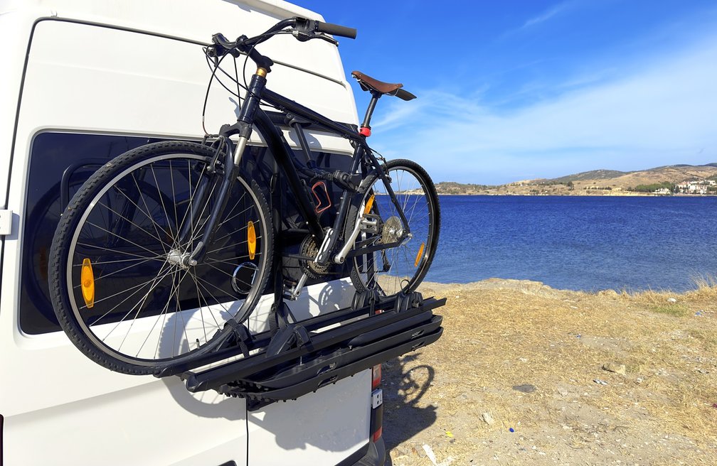 Zwei Fahrräder auf einem Heckträger an einem Wohnmobil, geparkt direkt am Meer unter blauem Himmel – Symbol für Campingurlaub, Flexibilität und Fahrradtransport beim Reisen.