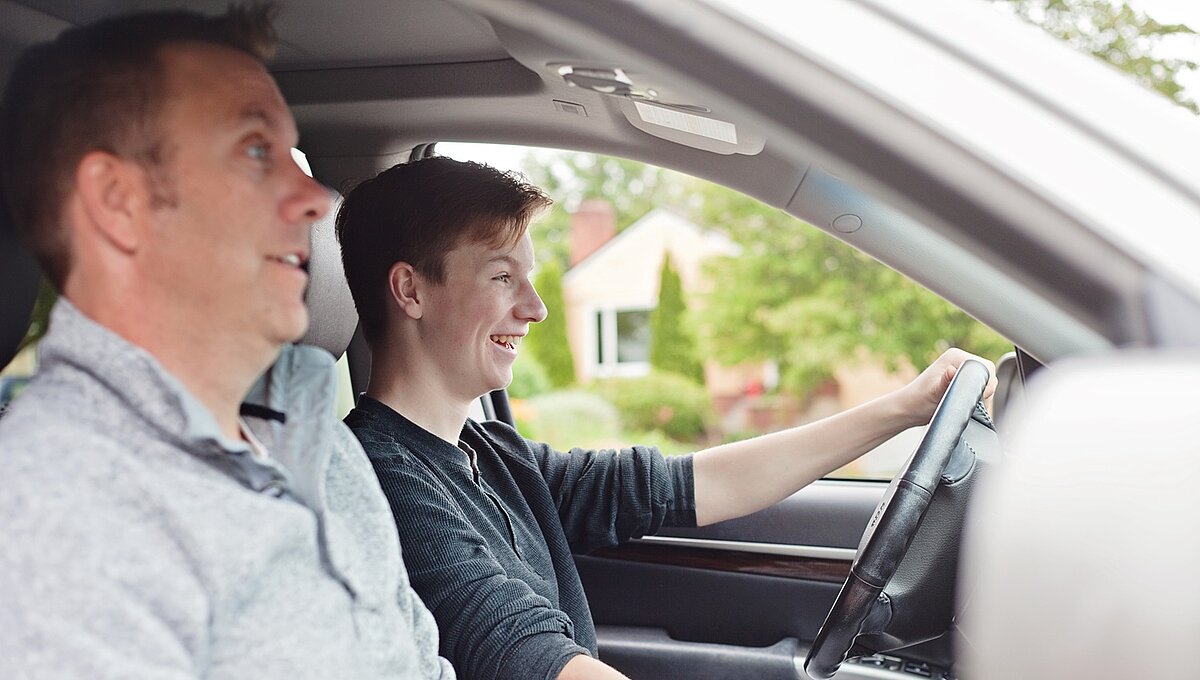 Vater sitzt auf dem Beifahrersitz und begleitet seinen Sohn beim Autofahren.
