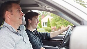 Vater sitzt auf dem Beifahrersitz und begleitet seinen Sohn beim Autofahren.