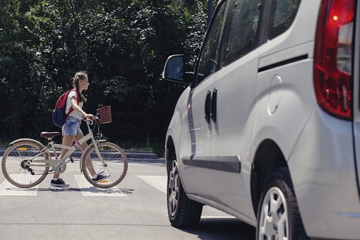 Ein Kind schiebt ihr Fahrrad über ein Zebrastreifen und ein weißes Auto wartet