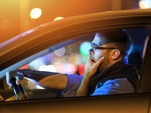 Ein Mann fährt im Dunkeln im Auto und gähnt