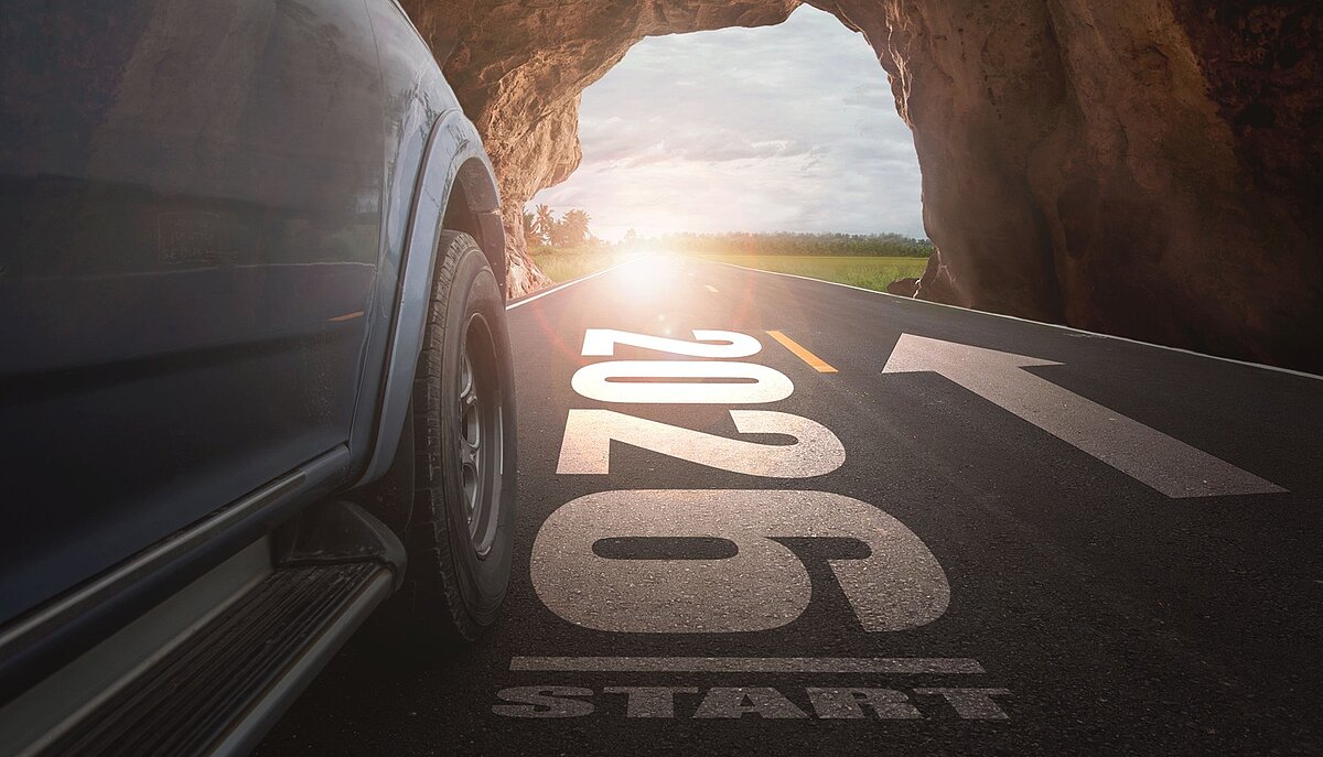 Blick aus einem dunklen Tunnel auf eine helle Straße mit der auf den Asphalt gemalten Aufschrift „2026“, die in Richtung Tageslicht und offener Landschaft führt; links ist ein Teil eines Fahrzeugs sichtbar.