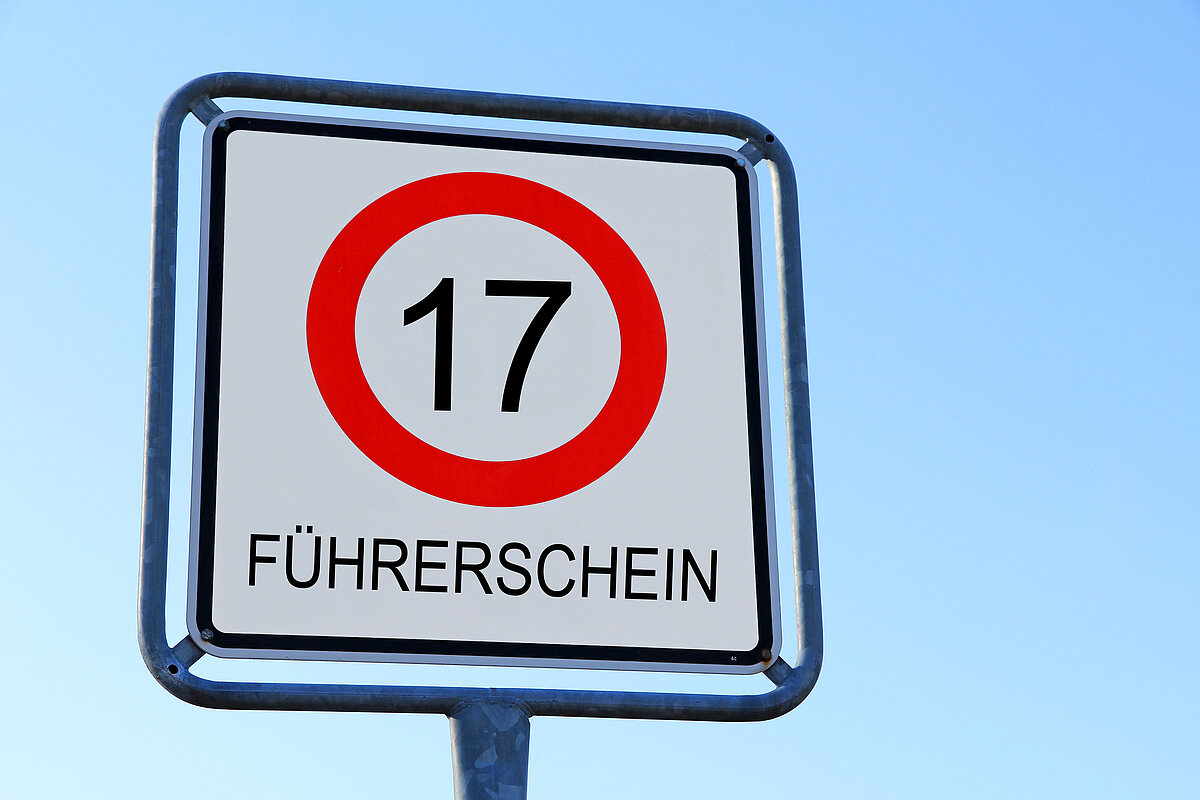 Ein Schild mit einer 17 in einem roten Kreis darunter steht Führerschein