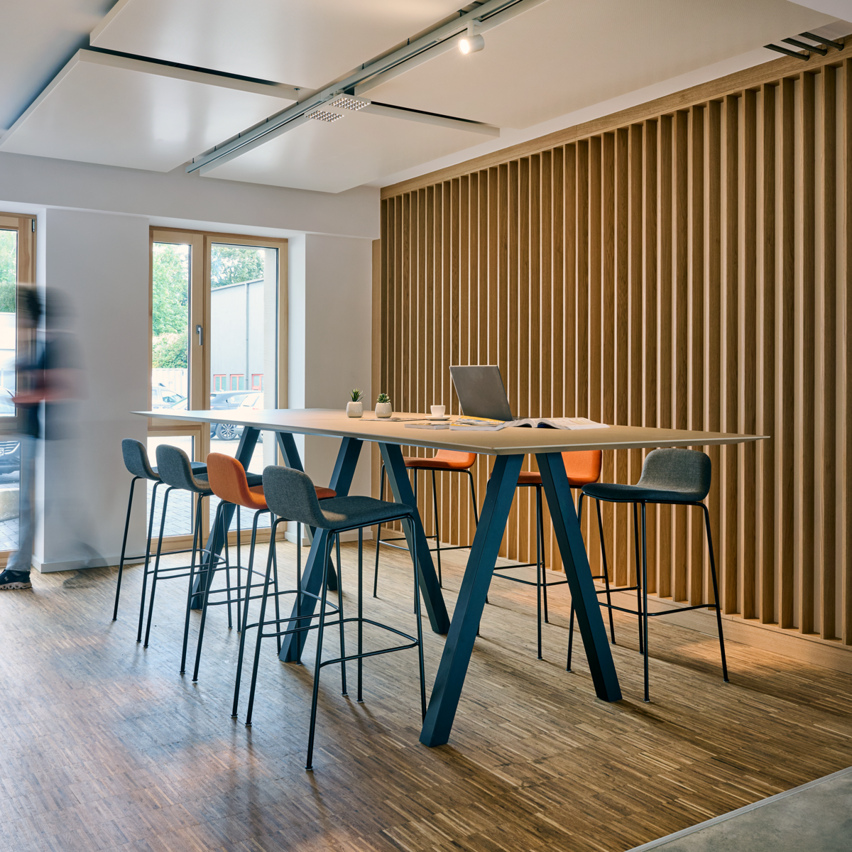 „Moderner Besprechungsraum mit großem Holztisch, Stühlen und Wandverkleidung aus Holzlamellen.“