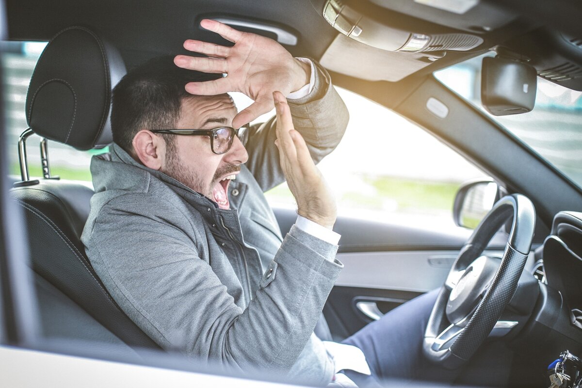 Ein Mann, der in einem Auto sitzt, sieht erschrocken aus, er hebt die Hände vor sein Gesicht, als wolle er sich schützen.
