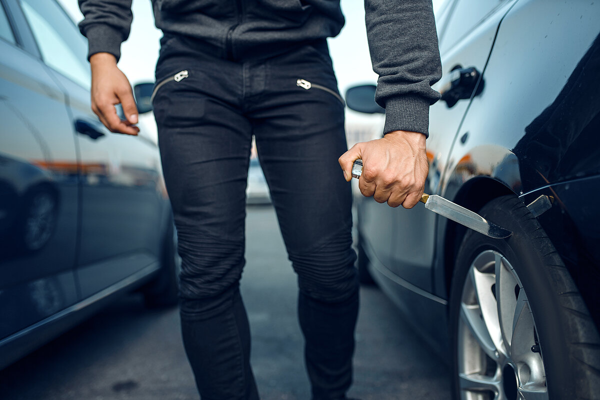 Ein Mann in dunkler Kleidung sticht Autoreifen platt