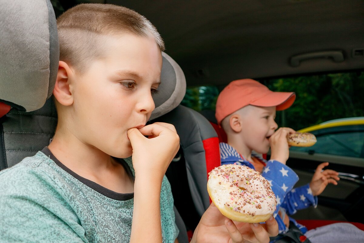 Zwei Jungen sitzen in Autositzen und essen Donuts.