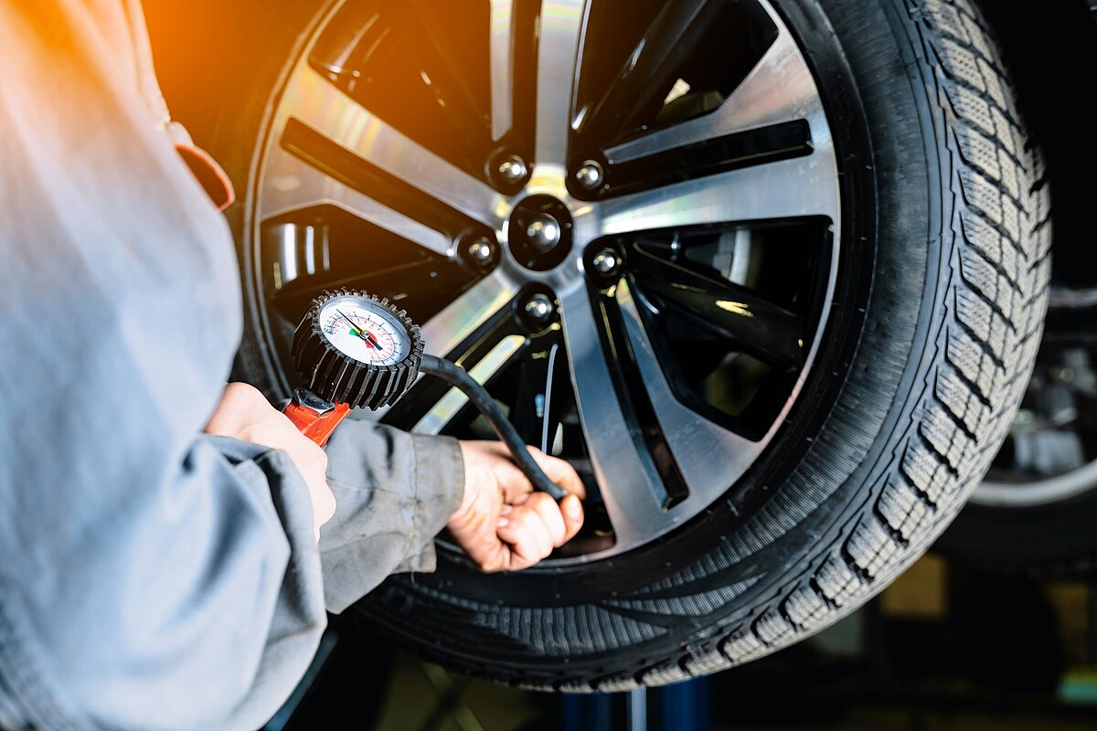 Mechaniker prüft den Luftdruck an einem montierten Autoreifen in der Werkstatt.