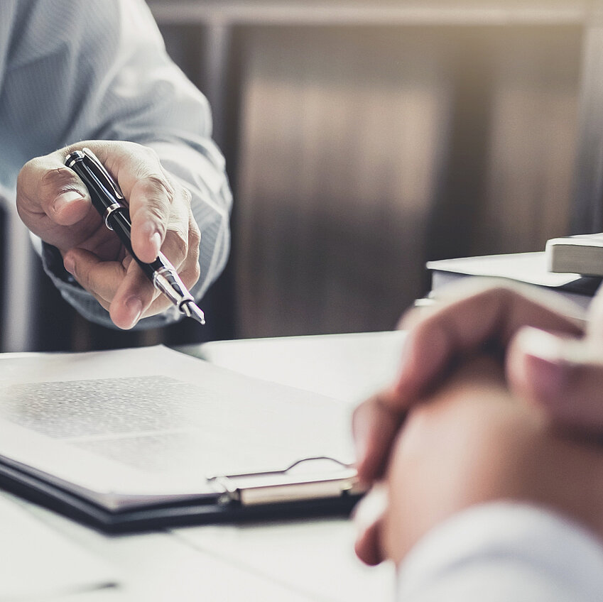 Nahaufnahme der Hände von 2 Personen die an einem Tisch gegenübersitzen, auf dem Dokumente liegen