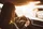 Eine Person mit langen Haaren fährt bei Sonnenuntergang mit dem Auto; das Sonnenlicht strömt durch das Fenster und spiegelt sich auf dem Armaturenbrett wider, wodurch im Innenraum ein warmer Schein entsteht.