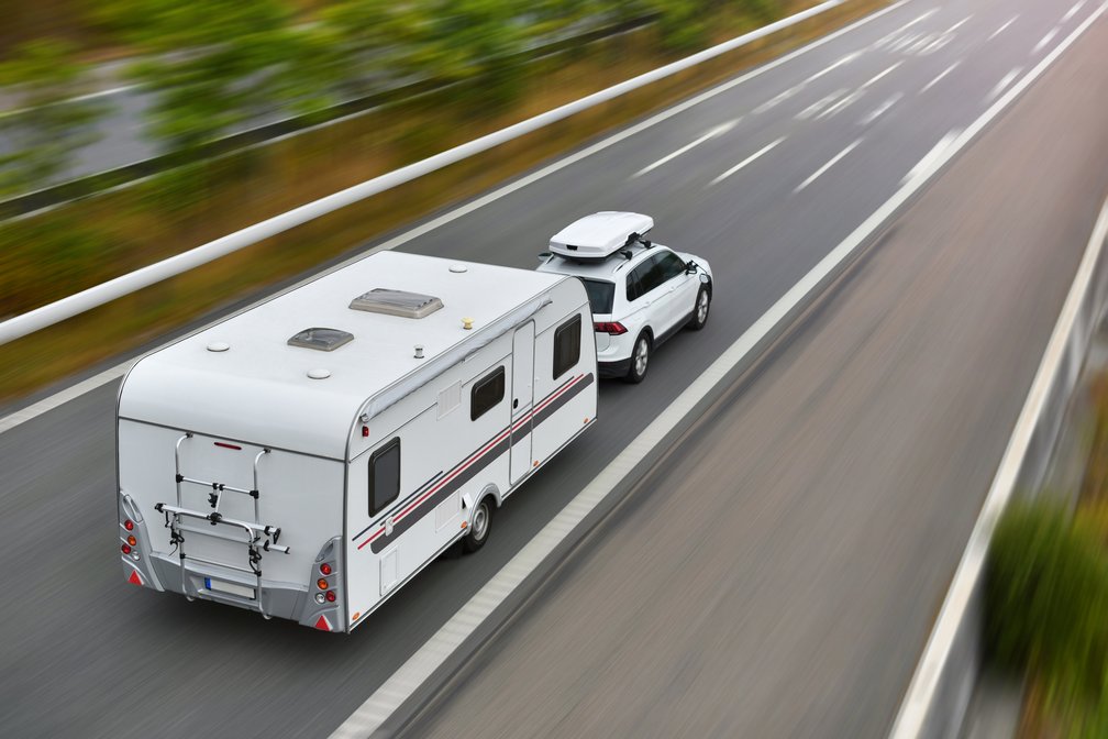Ein weißes Auto fährt mit einem Gespann über die Autobahn