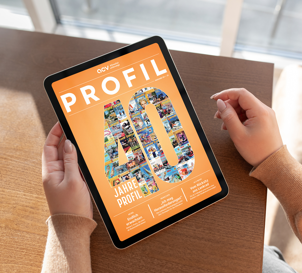 Eine Person hält ein Tablet in der Hand, auf dem die Titelseite einer Zeitschrift mit dem Titel PROFIL mit der Aufschrift 40 Jahre PROFIL auf orangefarbenem Hintergrund abgebildet ist. Die Zahl 40 ist mit einer Collage aus kleinen Fotos gefüllt.
