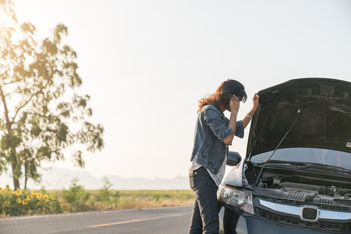 Eine Frau steht am Straßenrand und hat eine Panne mit ihrem Auto