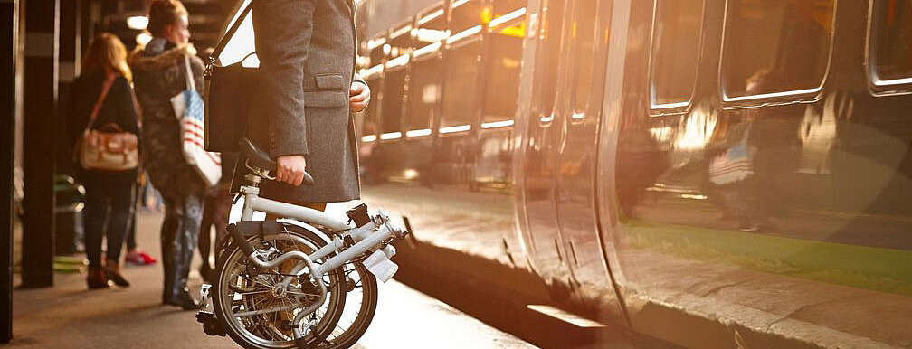Mann mit einem Klapprad am Bahnhof