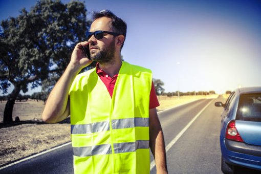 Mann trägt eine Warnweste und telefoniert aufgrund einer Autopanne