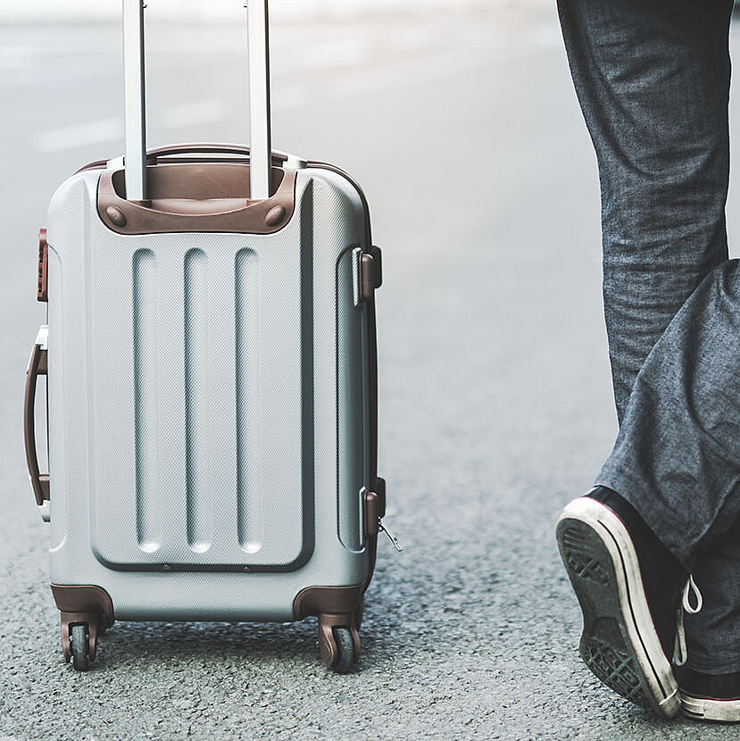 Eine Person steht neben einem Rollkoffer auf der Straße