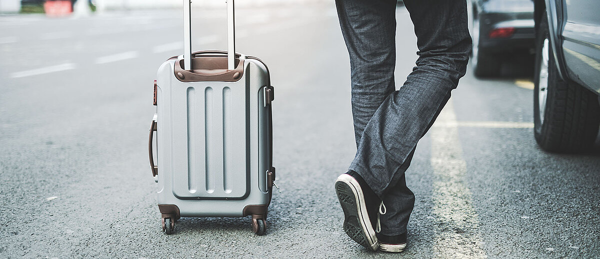 Eine Person steht neben einem Rollkoffer auf der Straße