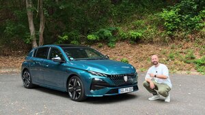 Ein Mann hockt neben einem blauen Fließheckwagen, der auf einer gepflasterten Fläche geparkt ist; im Hintergrund sind grüne Bäume und Büsche zu sehen.