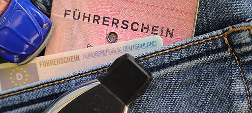 Alter rosa Papierführerschein und neuer EU-Kartenführerschein stecken in einer Jeans-Tasche, daneben ein Autoschlüssel und ein kleines blaues Spielzeugauto.