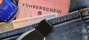 Alter rosa Papierführerschein und neuer EU-Kartenführerschein stecken in einer Jeans-Tasche, daneben ein Autoschlüssel und ein kleines blaues Spielzeugauto.