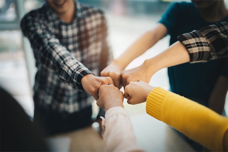 Fünf Menschen führen die Hände in die Mitte zusammen