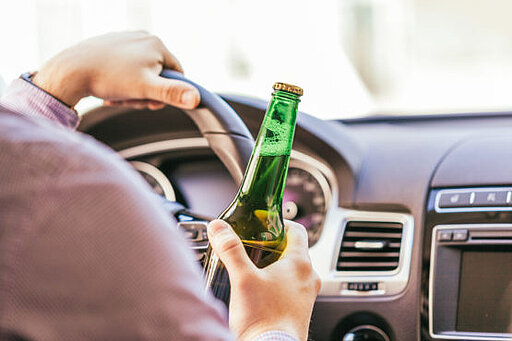 Mann sitzt in einem Auto und hält eine Bierflasche in der Hand