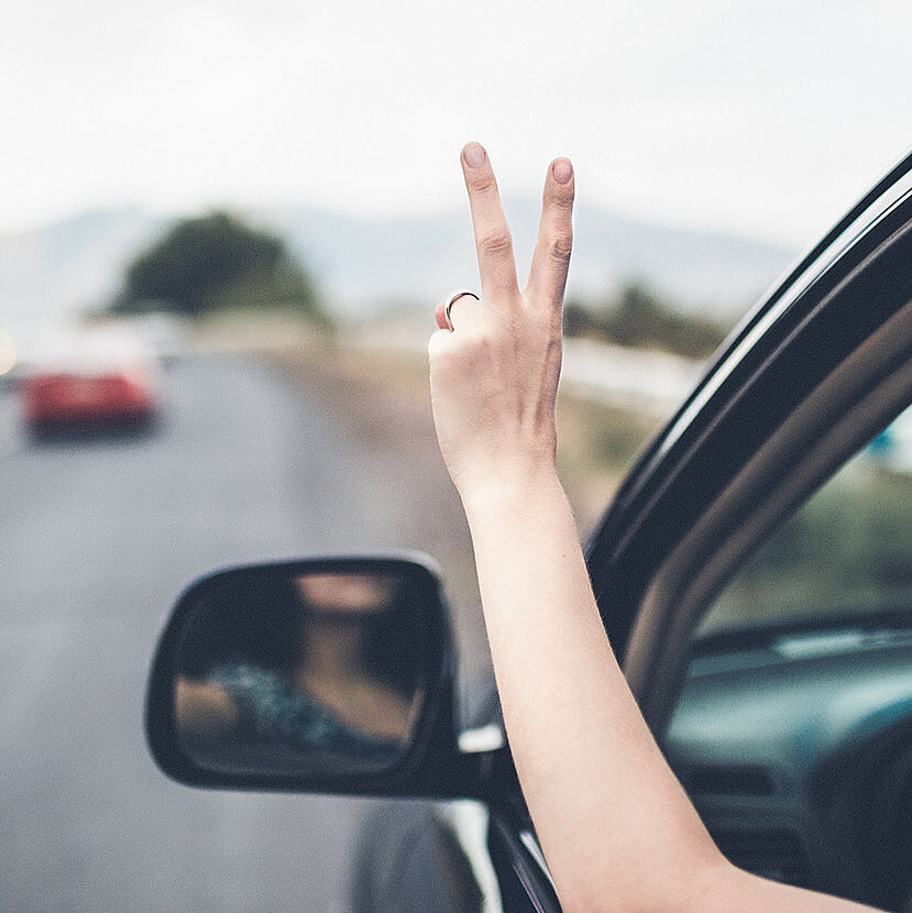 Eine Person sitzt im Auto und hält ihre Hand aus dem Fenster