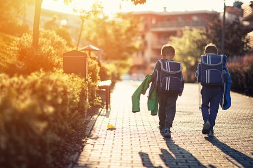 zwei Kinder gehen nebeneinander zur Schule