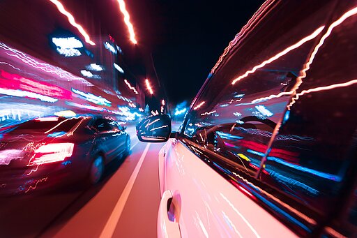 Illegales Straßenrennen bei Nacht mit schnellen Autos, Lichtspuren und urbaner Szenerie – dynamische Langzeitbelichtung auf nächtlicher Straße.