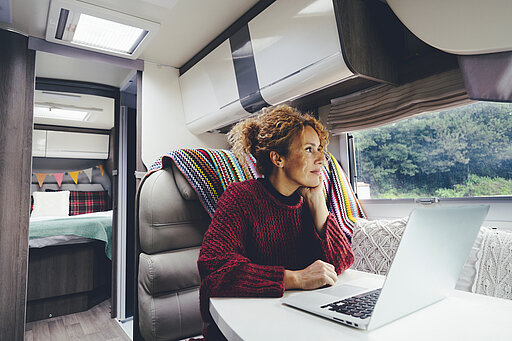 Eine Frau sitzt an Ihrem Laptop in einem Wohnmobil