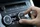 Eine Hand dreht den Drehregler „AUTO A/C“ am Bedienfeld der Klimaanlage eines Autos; auf dem digitalen Display ist die auf 24,0 °C eingestellte Temperatur zu sehen, und verschiedene Tasten für Luftstrom und Gebläsestufe sind sichtbar.