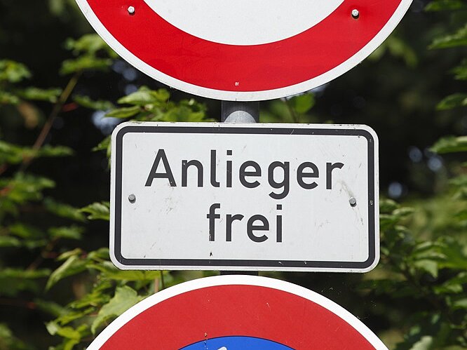 Verkehrszeichen 'Durchfahrt verboten' (rotes rundes Schild mit weißer Mitte) mit Zusatzschild 'Anlieger frei' (weißes rechteckiges Schild mit schwarzer Schrift). Bedeutet: Allgemeines Fahrverbot, aber Anlieger mit berechtigtem Anliegen dürfen passieren.