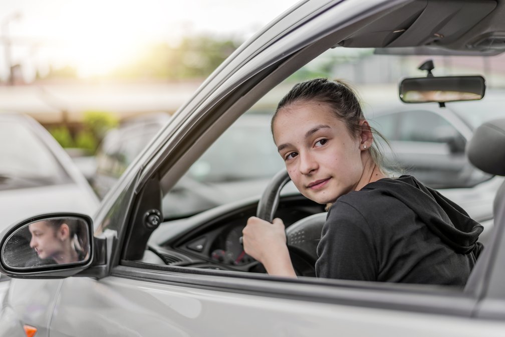 Junge Frau sitzt am Steuer eines Autos, blickt konzentriert über die Schulter nach hinten