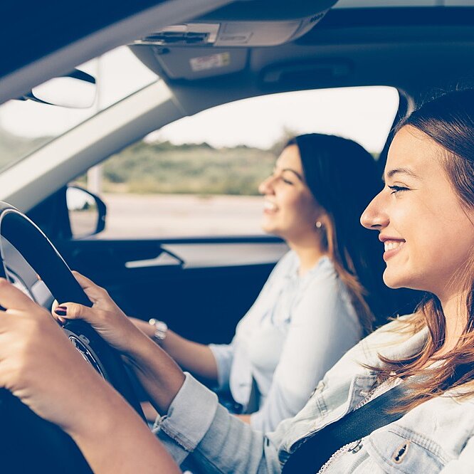 2 junge Frauen sitzen lächelnd in einem Fahrzeug