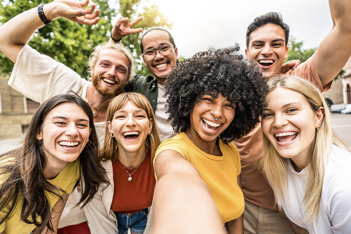 Multikulturelle Freunde, die draußen gemeinsam in die Kamera lächeln