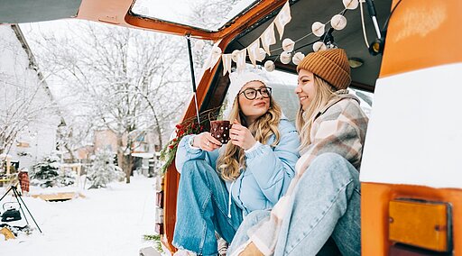 Zwei Freundinnen sitzen im Wohnmobil beim Wintercamping