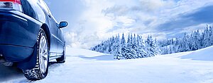 Auto mit Winterreifen fährt auf verschneiter Straße durch winterliche Landschaft mit Tannen und Schnee.