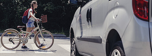 Ein Kind schiebt ihr Fahrrad über ein Zebrastreifen und ein weißes Auto wartet