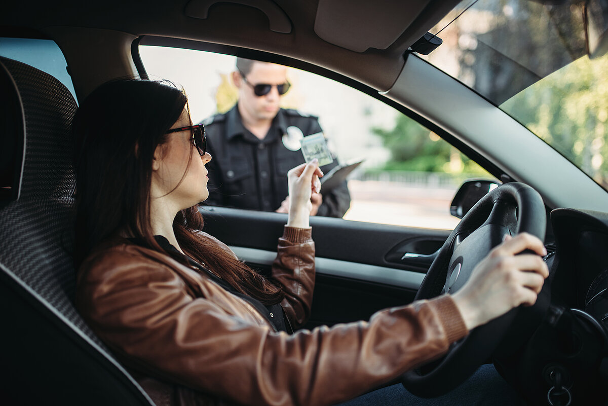 Frau sitzt im Auto und gibt einer Polizistin ihren Führerschein