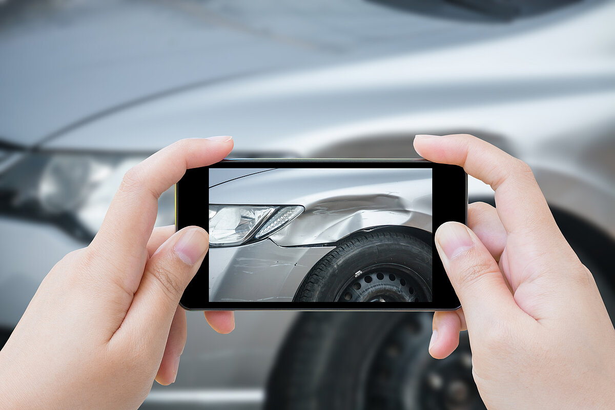 Person fotografiert Unfallschaden am Auto