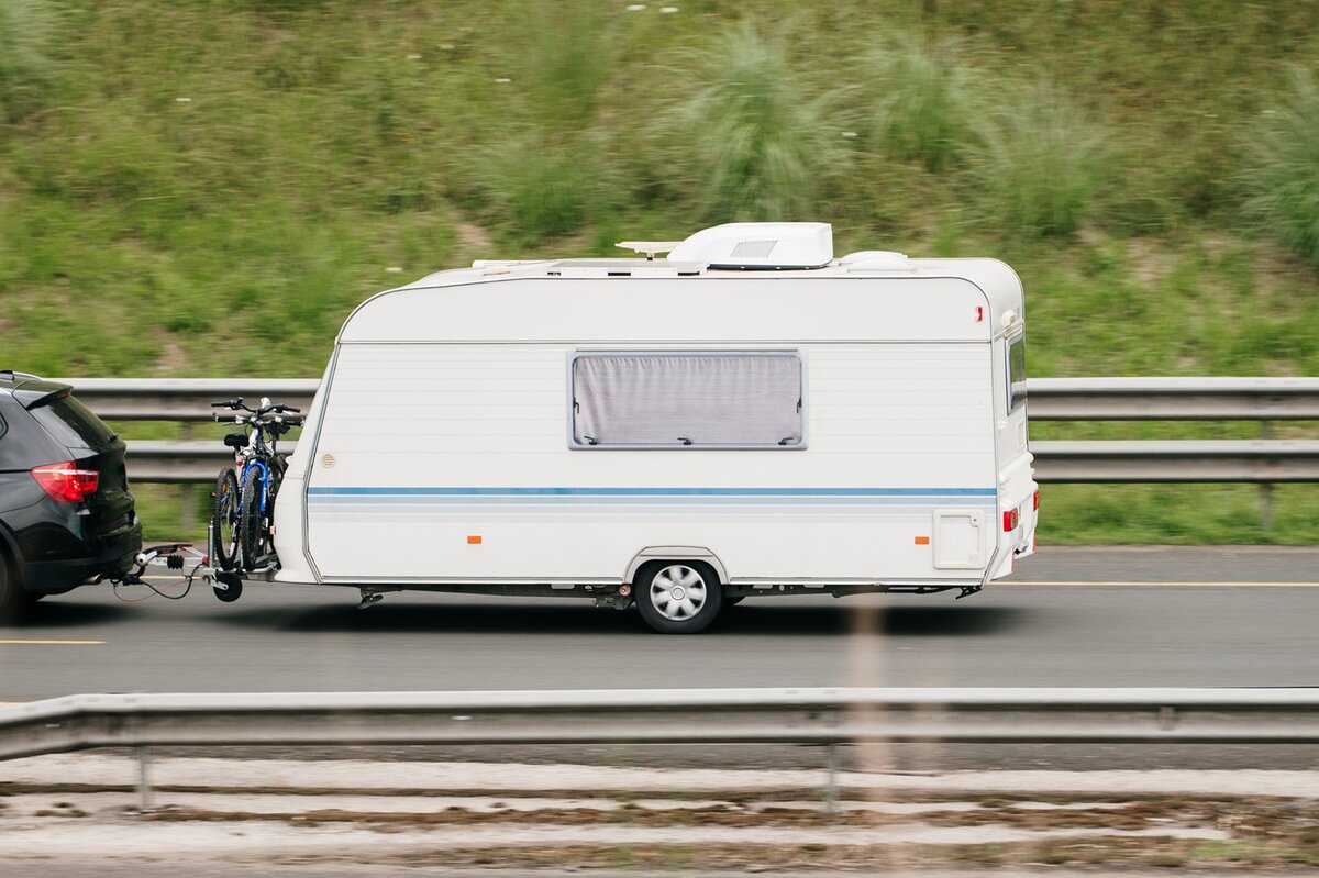 Ein schwarzes Auto zieht einen weißen Wohnwagen über eine Straße. 