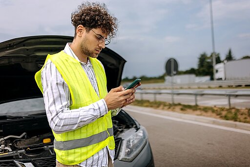 Mann steht mit einer Warnweste vor einem Auto mit einer Panne