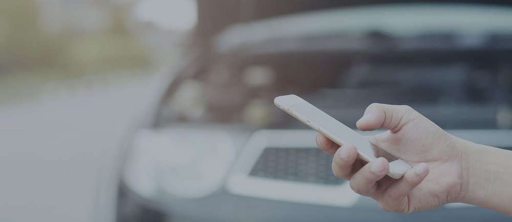 Eine Person hat eine Panne mit ihrem Auto und hält das Handy in der Hand 
