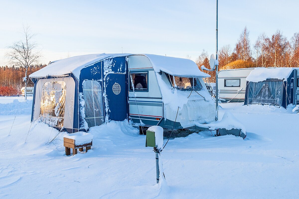 Wohnmobil mit Vorzelt steht beim Wintercamping auf verschneitem Stellplatz