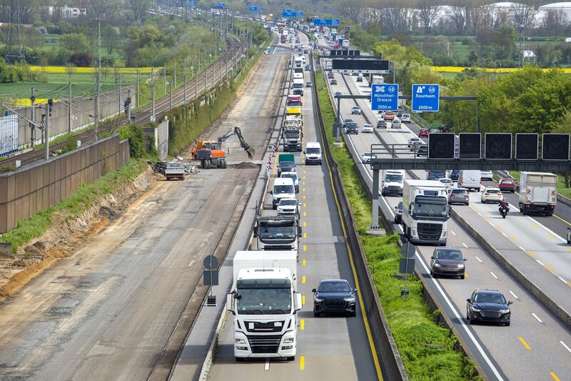 Eine lange Reihe von Fahrzeugen steht auf einer Autobahn im Stau, auf der einen Seite sind Bauarbeiten und Maschinen zu sehen. Auf den gegenüberliegenden Fahrspuren ist der Verkehr weniger dicht und fließt freier.
