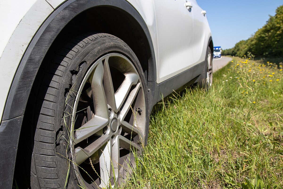 Auto steht am Straßenrand, ein Reifen ist stark beschädigt.