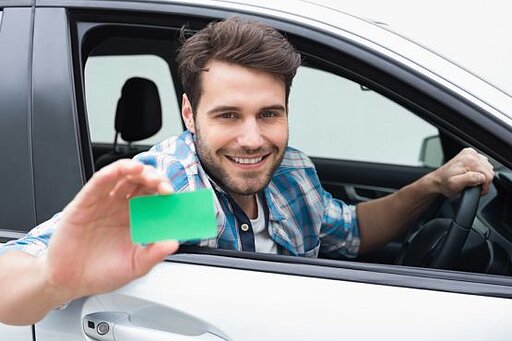 Ein Mann sitzt im Auto und hält eine grüne Karte hinaus