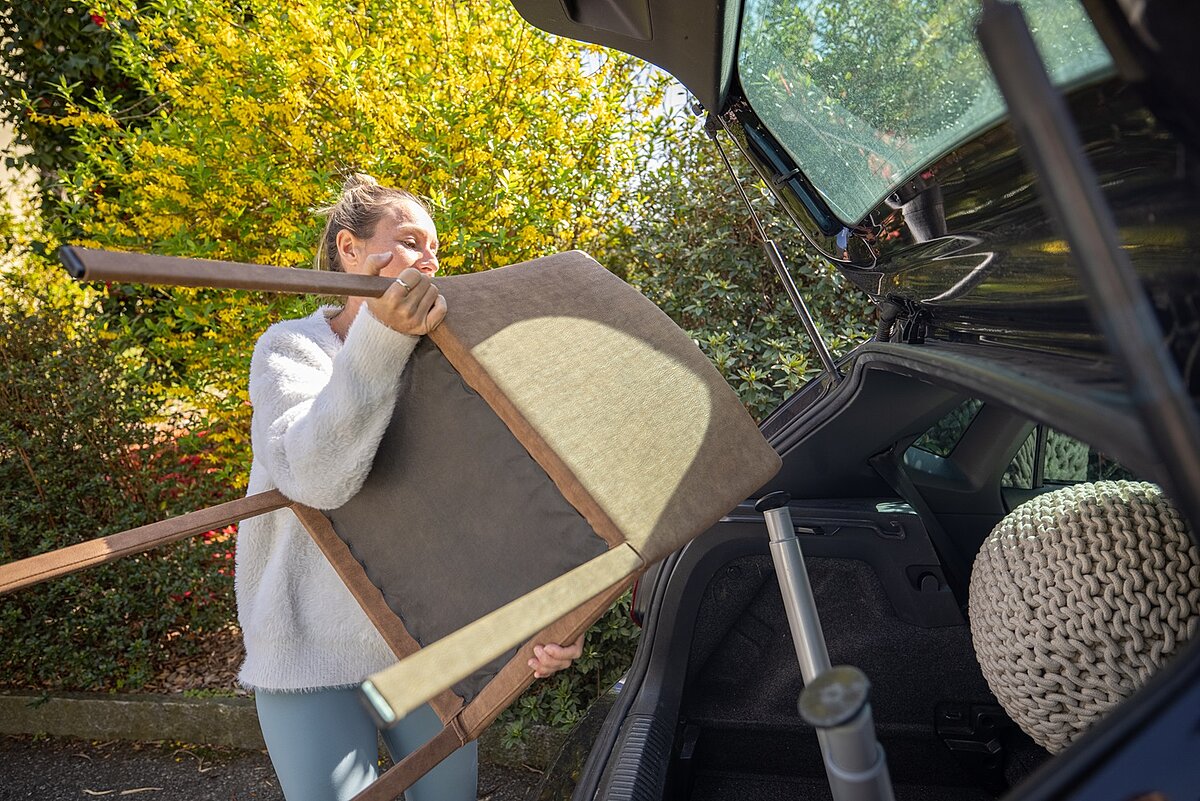 Frau verstaut Möbel und einen Stuhl im Kofferraum eines Autos im Garten.