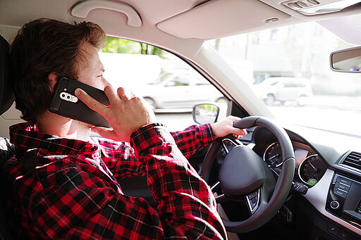 Mann sitzt im Auto und hat ein Handy am Ohr